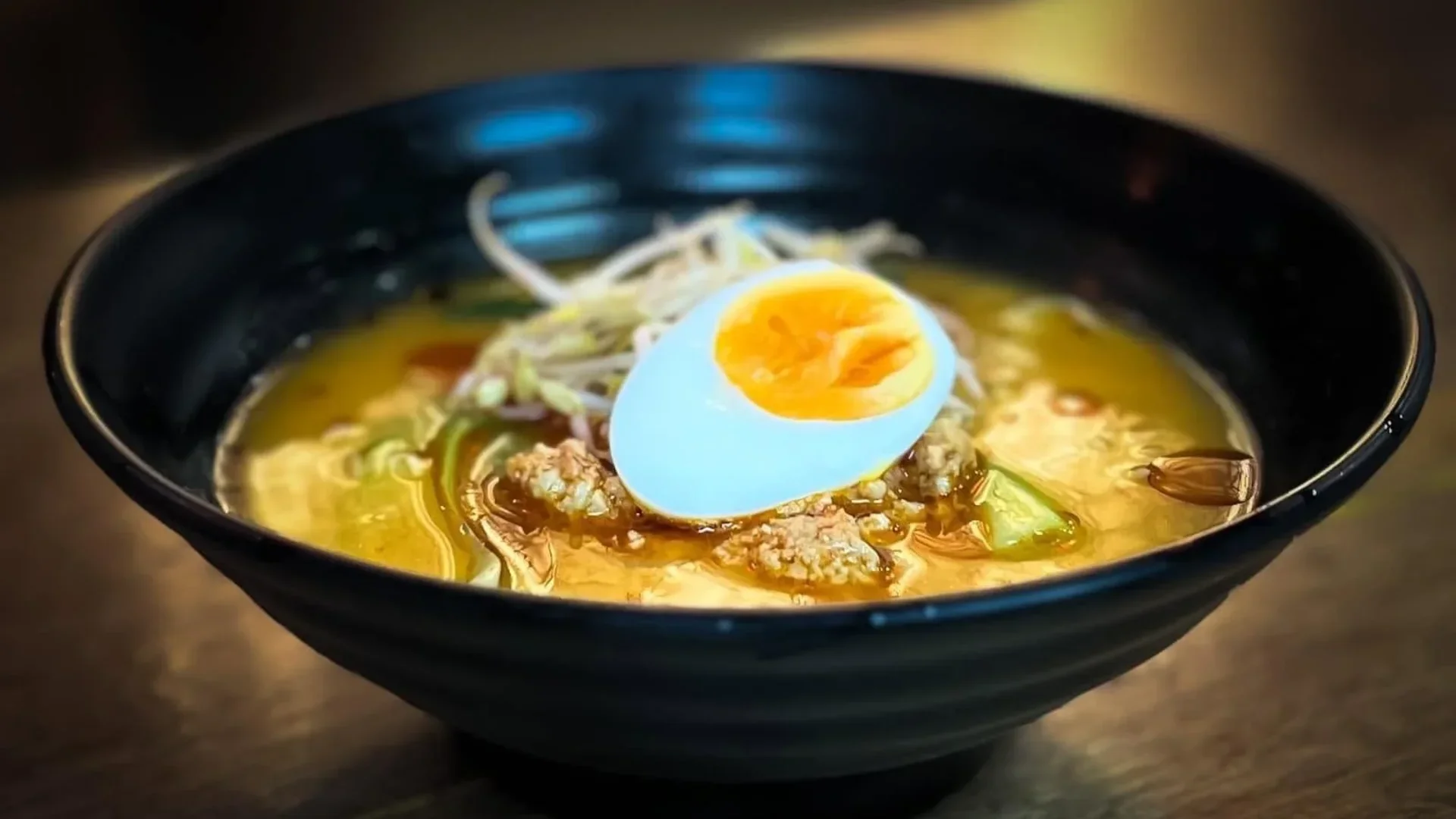 Bowl of Japanese ramen topped with a soft-boiled egg, minced meat, bean sprouts, and vegetables in a rich broth.