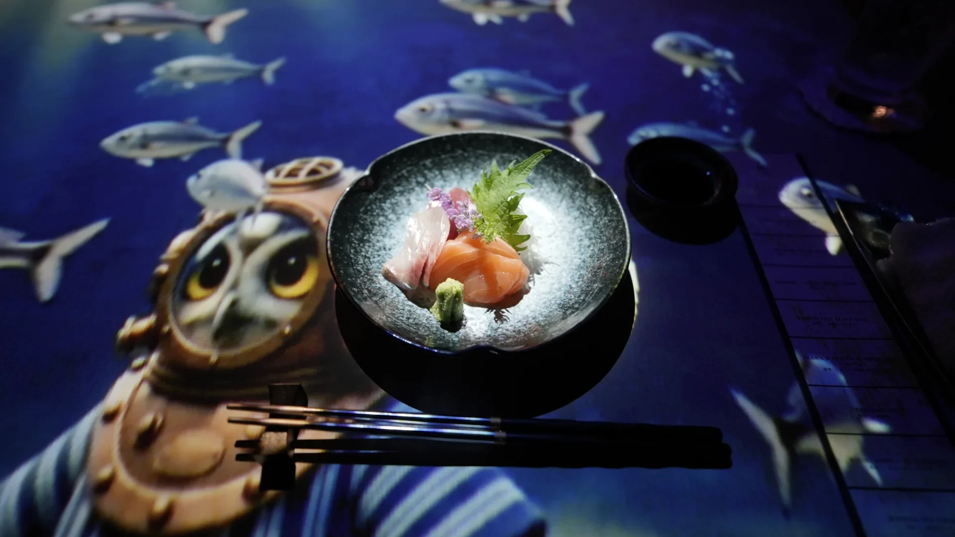 Salmon and white fish sashimi served with wasabi and shiso during an immersive underwater projection-mapping dining experience.