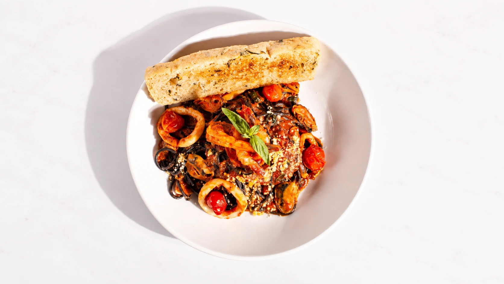 Black seafood pasta with shrimp, squid, mussels, cherry tomatoes, basil, and grated cheese, served with garlic bread.