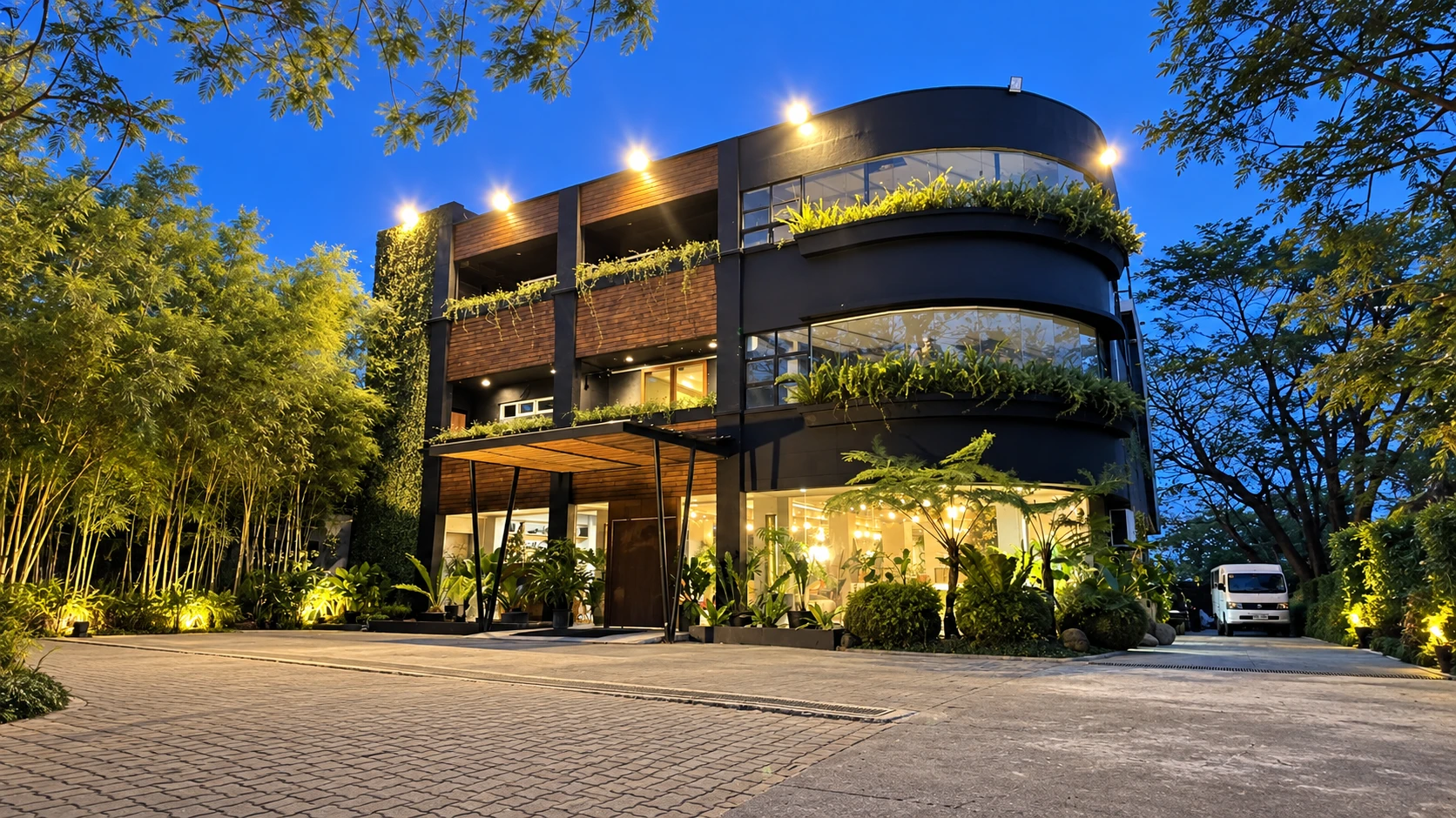 Exterior of TFG Hotel at dusk, featuring modern architecture, warm lighting, curved glass windows, and lush surrounding greenery.