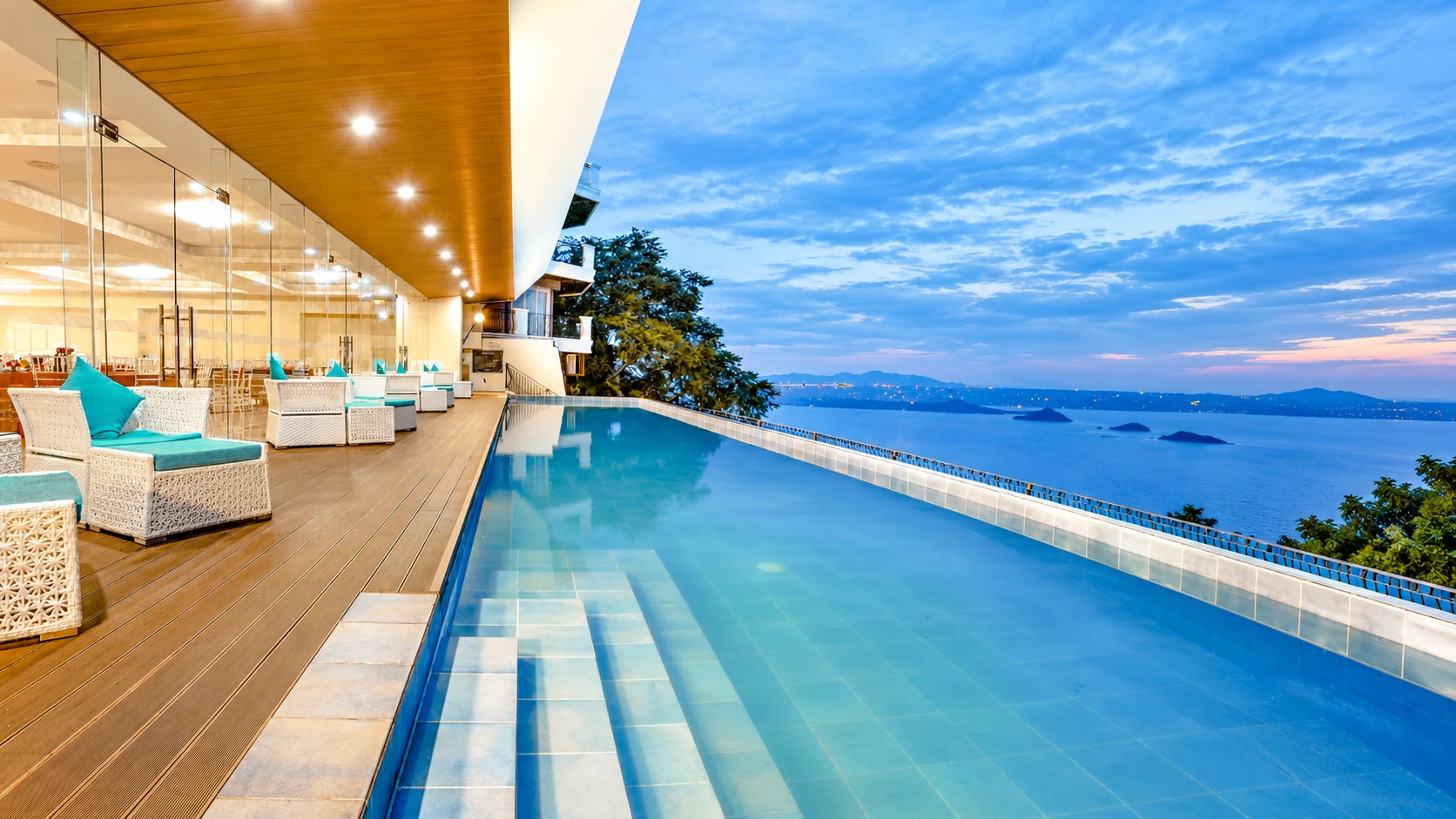 Infinity pool and outdoor lounge at The Lake Hotel Tagaytay overlooking Taal Lake and its surrounding mountains at sunset.