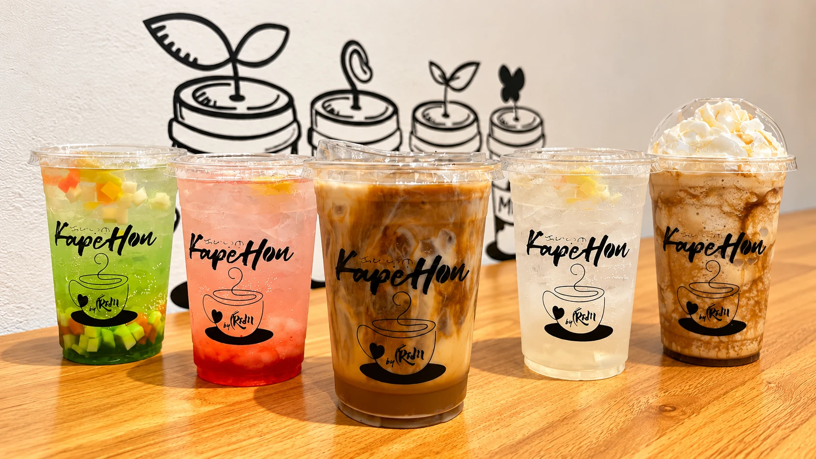 Iced creamy coffee from KapeHon served on a wooden counter against a playful tea and milk wall illustration.